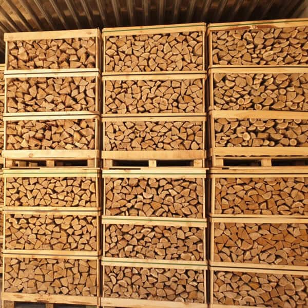 De Ovengedroogd Eikenhout Jumbopallet | Topkwaliteit Stookhout vormt een prachtig geheel, met stapels netjes gerangschikt ovengedroogd eikenhout die houten kratten tot de nok toe vullen. Onder een gegolfd metalen dak getuigen deze jumbopallets van precisie en ordelijkheid.