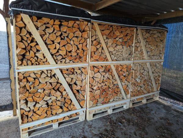 Jumbopallet Ovengedroogd Mix Haardhout, met Eik, Berk & Els houtstukken, wordt netjes gehakt en gestapeld in houten kratten. Deze worden op jumbopallets geplaatst onder een afdak met een zeil eroverheen ter bescherming tegen regen. De verschillende kleuren geven verschillende soorten of veroudering van het hout aan.